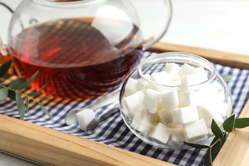 Refined sugar cubes in glass bowl and tongs on wooden tray