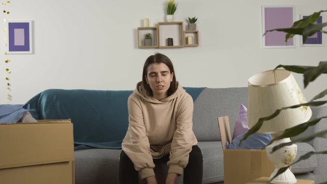 Upset young woman sitting on sofa near cardboard boxes