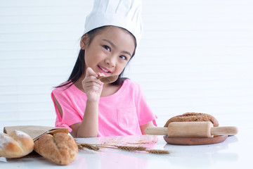 Happy little girl with chef hat and and bread on the table, white background