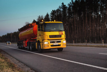 Fototapeta na wymiar A truck carries a tank of combustible fuel on a highway against a forest and blue sky. The concept of transportation of dangerous goods on the road, license