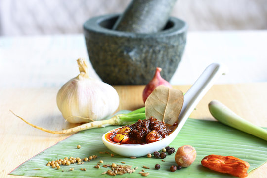Thai massaman curry paste in spoon with ingredients on table and mortar as background
