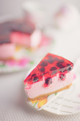 Currant cheesecake slice in floral spatula and saucer on a white table. Cheese cake with berries closeup, side view.