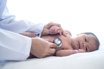 Doctor with stethoscope listening to heartbeat of newborn baby