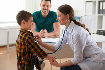 Father and son visiting pediatrician. Doctor examining little patient with stethoscope in hospital
