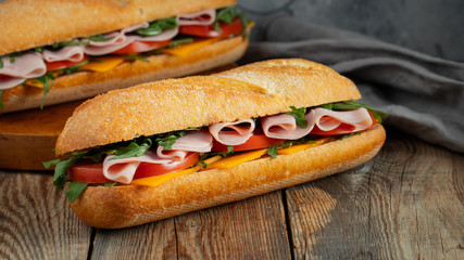 Two Long baguette Sandwiches with arugula, slices of fresh tomatoes, ham and cheese