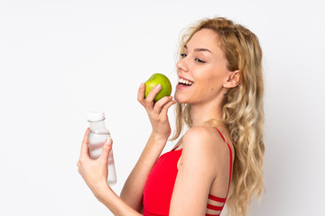 Young blonde woman isolated on white background with an apple and with a bottle of water