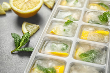 Ice cubes with lemon and mint in tray on grey table, closeup