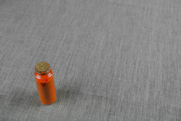 Red powder and crystalls crystals in small bottle on gray linen background