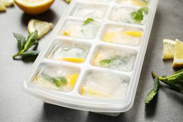 Ice cubes with lemon and mint in tray on grey table, closeup