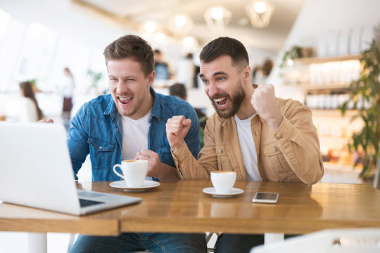 two handsome men friends watching online game cheering on their favourite team, looking excited, hobby and time spanding