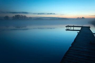Fototapeta na wymiar Foggy blue evening at the lake with a long bridge