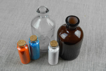Blue, red and white powder and crystalls crystals in small bottles on gray linen background