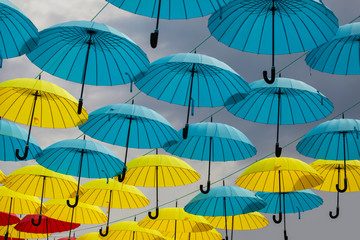 Yellow and blue umbrellas against a cloudy sky. Colorful umbrellas background. Colorful umbrellas in the sky. Street decoration.