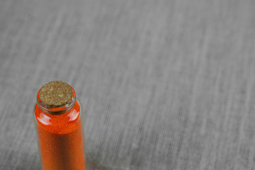 Red powder and crystalls crystals in small bottle on gray linen background