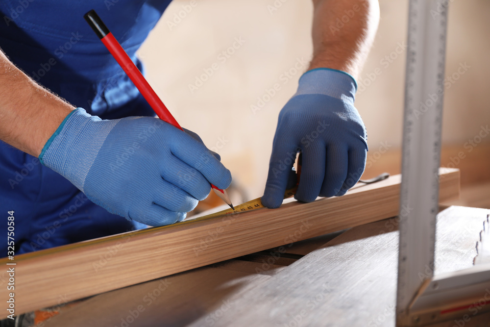 Wall mural Professional carpenter making mark on wooden bar in workshop, closeup