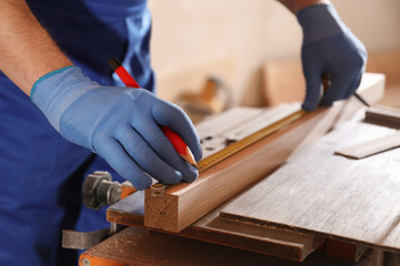 Professional carpenter measuring wooden bar in workshop, closeup