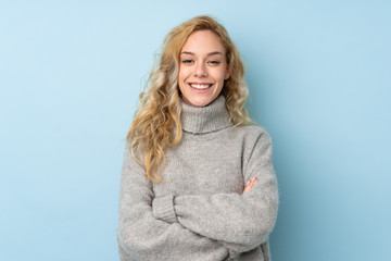 Young blonde woman wearing a sweater isolated on blue background keeping the arms crossed in...