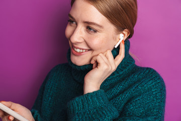 Photo of smiling caucasian woman using wireless earphone and cellphone