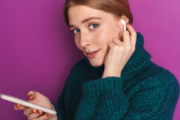 Photo of pleased caucasian woman using wireless earphone and cellphone