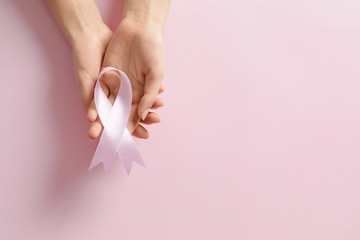 Woman holding pink ribbon on color background, top view with space for text. Breast cancer awareness