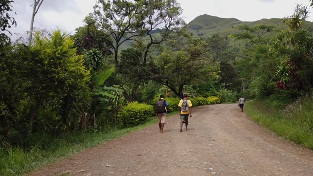 Two young people walking with their backpacks in a village in Papua New Guinea. Slowmotion.