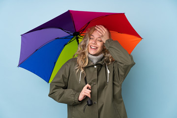 Young blonde woman holding an umbrella isolated on blue background has realized something and intending the solution