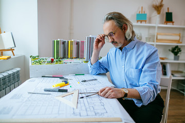 Fototapeta na wymiar thoughtful caucasian senior architect working in office with drawings, using different stationery. professional architect sit thinking, have brainstorm time