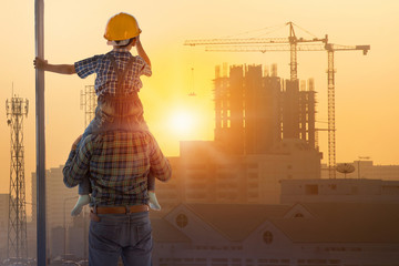 Asian boy on father's shoulders with background of new high buildings and silhouette construction...