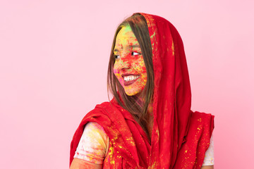 Young Indian woman with colorful holi powders on her face isolated on pink background happy and smiling