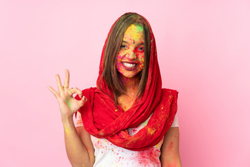 Young Indian woman with colorful holi powders on her face isolated on pink background showing ok sign with fingers