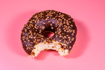 Bitten donut with chocolate glaze on top isolated on a pink background