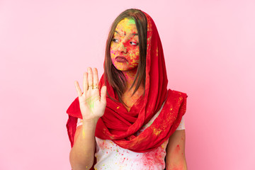 Young Indian woman with colorful holi powders on her face isolated on pink background making stop gesture and disappointed