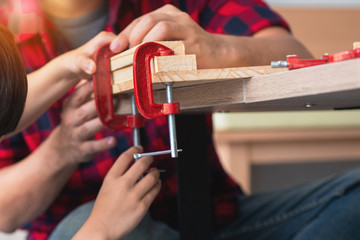 Close up little boy hand and father using a C clamp in his workshop, father and son concept