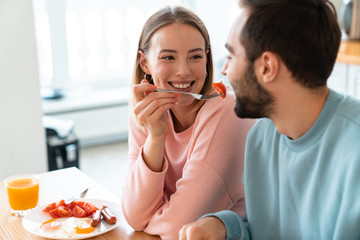 Portrait of young happy couple eating together while having breakfast