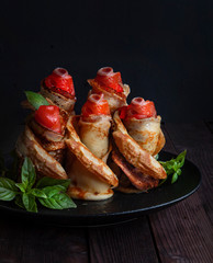 Rolls of pancakes with salmon, goat cheese, in the shape of a flower. Dark wooden table.