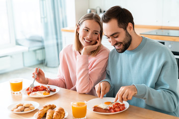 Obraz na płótnie Canvas Portrait of young happy couple eating together while having breakfast