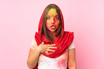 Young Indian woman with colorful holi powders on her face isolated on pink background surprised and shocked while looking right