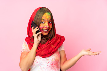 Young Indian woman with colorful holi powders on her face isolated on pink background keeping a conversation with the mobile phone with someone