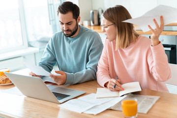 Portrait of young irritated couple working with laptop and documents