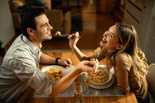 Happy Couple In Love Sharing Food At Dining Table.
