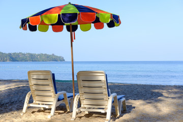 Beach bed and cheerful colorful parasol on tropical beach with blue sky and blue sea.