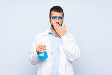 Young scientific holding laboratory flask over isolated background covering mouth with hands