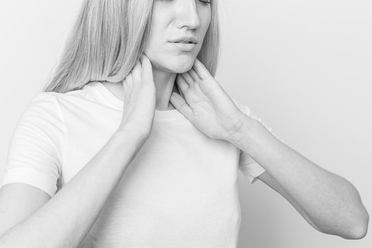 Female checking thyroid gland by herself. Close up of woman in white t- shirt touching neck with red spot. Thyroid disorder includes goiter, hyperthyroid, hypothyroid, tumor or cancer Health care.