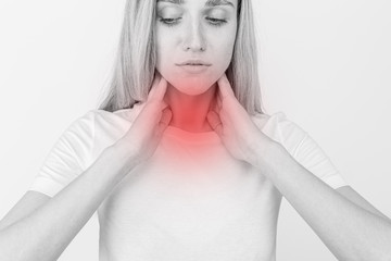 Female checking thyroid gland by herself. Close up of woman in white t- shirt touching neck with...
