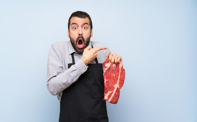 Chef holding a raw meat surprised and pointing side