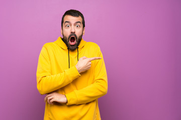 Handsome man with yellow sweatshirt surprised and pointing finger to the side