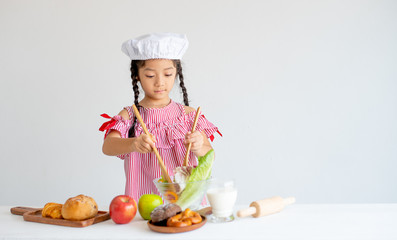 Asian little chef use wood ladle mix salad in glass bowl with white background.