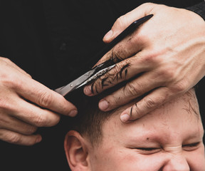 Hairdresser cuts the hair of a boy with scissors