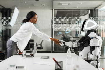 smiling african american businesswoman shaking hands with robot in office