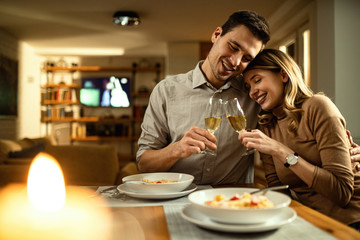 Young affectionate couple toasting with Champagne during a meal in dining room.